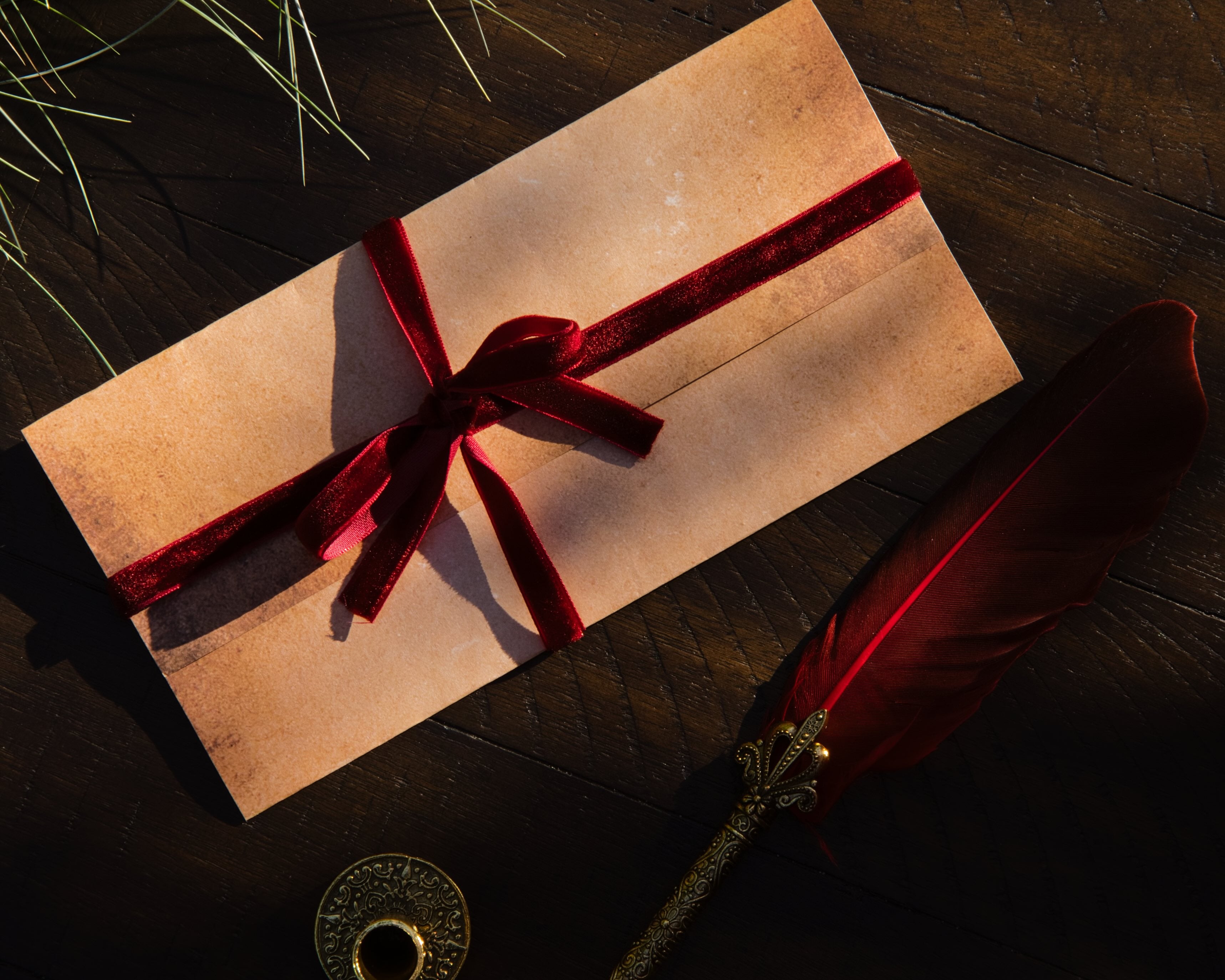 Envelope tied with a red ribbon on a dark surface with a feather pen and seal.
